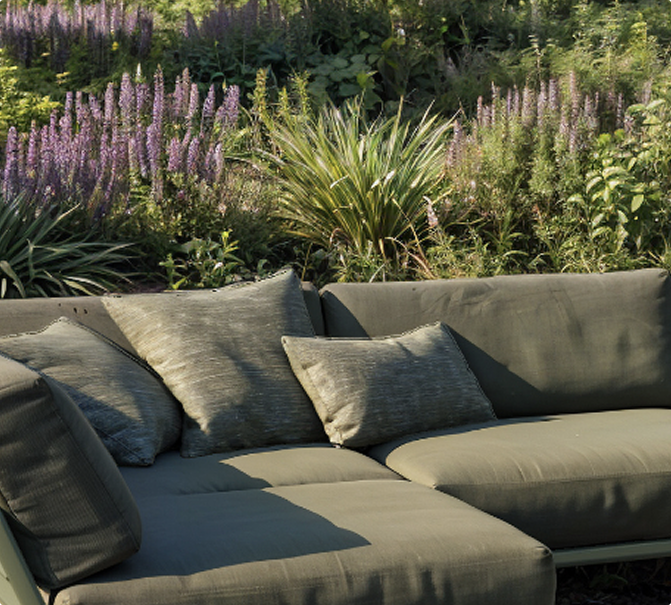 Elegante Outdoor-Lounge mit Kissen vor üppig blühendem Garten